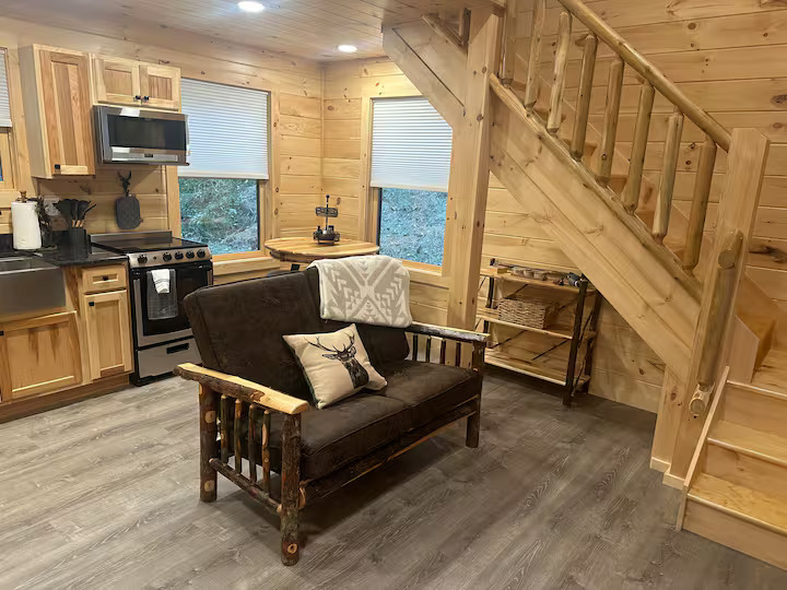 Cabin living room with futon sofa, stairs to loft, and kitchen